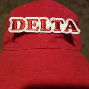 May include: Red baseball cap with a white and red embroidered patch that says "DELTA"