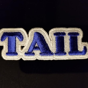 Op de afbeelding: Witte geborduurde patch met het woord "TAIL" in blauwe letters.