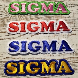 Könnte beinhalten: Vier gestickte Aufnäher mit dem Wort "SIGMA" in verschiedenen Farben. Die Aufnäher befinden sich auf einem weißen Holzhintergrund. Die Farben sind rosa, rot, blau und gelb.