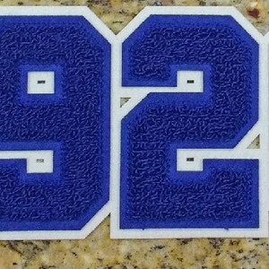 Pode incluir: Patch de aplique de feltro azul com contorno branco em forma de número 1920. O patch tem um símbolo de marca registrada no canto superior direito.