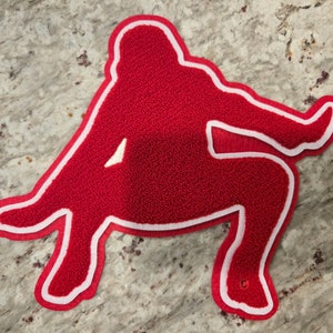 May include: Red felt outline of a person sitting with legs crossed, with white stitching around the edges.