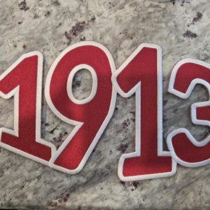 Op de afbeelding: Rode stoffen cijfers 1913 met witte rand. De cijfers zijn groot en vetgedrukt, met een textuur. De cijfers zijn waarschijnlijk bedoeld voor een knutselproject of decoratie.