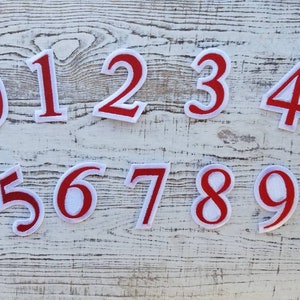 May include: A collection of ten embroidered number patches, with digits 0 to 9. Each patch has a red border and a white centre, ideal for personalising clothing or craft projects.