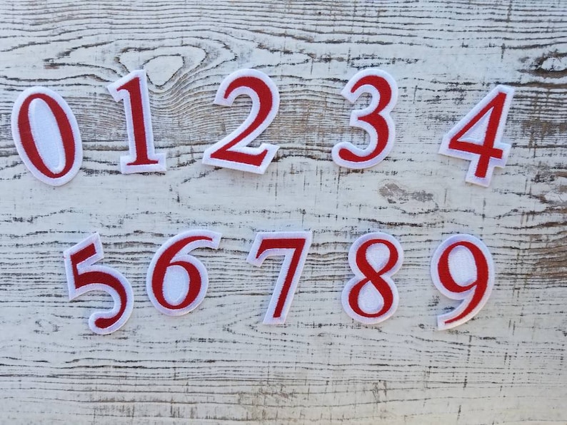 May include: A collection of ten embroidered number patches, with digits 0 to 9. Each patch has a red border and a white centre, ideal for personalising clothing or craft projects.