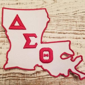 May include: A white patch in the shape of the state of Louisiana with red embroidered letters that spell out "ΔΣΘ".