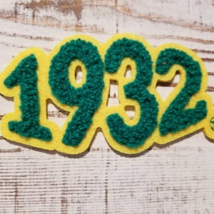 May include: A yellow felt patch with the year 1932 in green fuzzy letters. The patch has a small trademark symbol in the lower right corner.