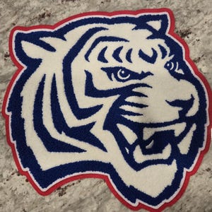 May include: A white tiger head with blue stripes and a red outline. The tiger is facing right and has a fierce expression.