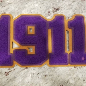 May include: Purple felt number 1911 with a gold outline. The numbers are in a large, bold font.