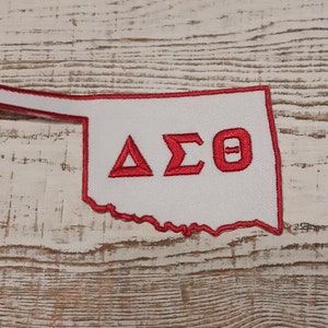 May include: White embroidered patch shaped like the state of Oklahoma with a red outline. The patch features the Greek letters Delta Sigma Theta in red.