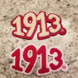 May include: Two felt patches with the number 1913 in white and red lettering. The top patch has white lettering on a red background. The bottom patch has red lettering on a white background. Both patches have a trademark symbol.