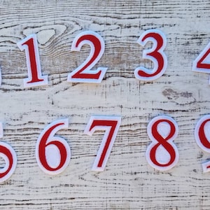 Puede incluir: Diez parches de plancha de fieltro rojo con contornos blancos, cada uno con un número del 0 al 9.