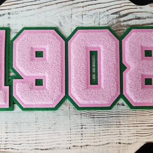 May include: Pink and green felt numbers, 1908, on a white wooden background.