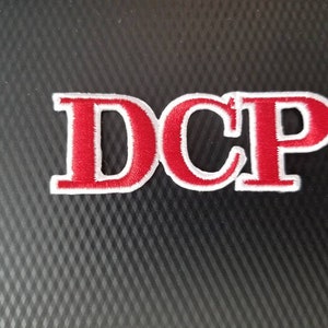 May include: Red embroidered patch with white outline spelling "DCP".
