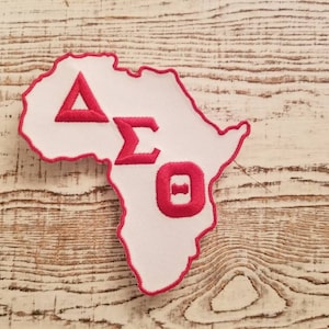 Op de afbeelding: Een witte omtrek van het Afrikaanse continent met een rode omtrek en de letters Delta Sigma Theta in rood binnen de omtrek.