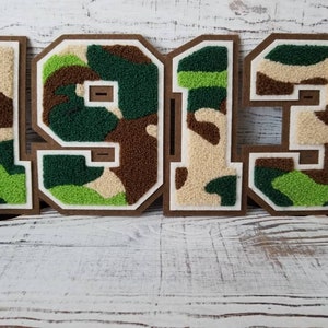 May include: A set of four felt patches in a camouflage pattern, forming the number 1913. The patches are brown, green, and beige.