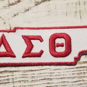 May include: White embroidered patch shaped like the state of Tennessee with the letters "ΔΣΘ" in red.