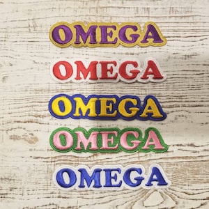May include: Five embroidered iron-on patches with the word "OMEGA" in different colours. The patches are in a row from top to bottom: purple, red, yellow, green, and blue.