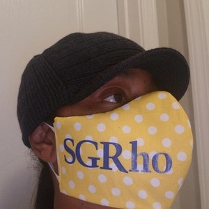 May include: A yellow face mask with white polka dots and blue text that says "SGRho".