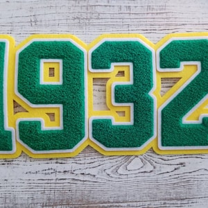 Op de afbeelding: Groene vilt applicatie cijfers 1932 met witte contouren en gele achtergrond.