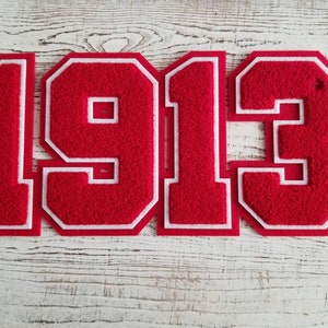 May include: Red felt applique numbers in the style of a sports jersey, spelling out the year 1913.