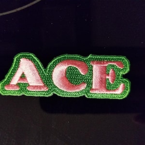 May include: A green and pink embroidered patch with the word "ACE" in pink letters.
