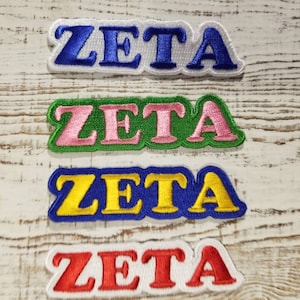 Könnte beinhalten: Vier gestickte Aufnäher mit dem Wort "ZETA" in verschiedenen Farben. Die Aufnäher sind weiß, grün, blau und rot.
