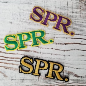 May include: Three embroidered patches with the word "SPR." in different colors. The patches are yellow with green, purple, and black outlines.