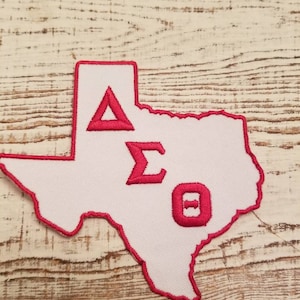 May include: White felt patch in the shape of the state of Texas with a red outline. The letters Delta Sigma Theta are embroidered in red on the patch.