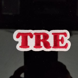 May include: Red embroidered patch with the word "TRE" in white outlined letters.