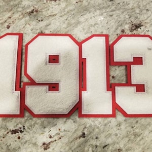 May include: Red felt applique numbers in a white font, spelling out the year "1913".
