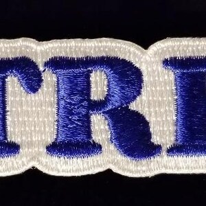 Könnte beinhalten: Weißer Filz-Patch mit dem Wort "TRE" in blau gestickt.