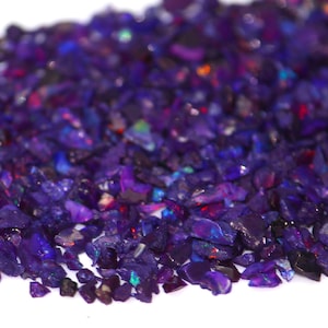 May include: A pile of small, iridescent purple opal chips. The chips are various shapes and sizes, and they have a shimmering, rainbow-like effect.