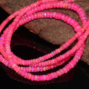 May include: Several strands of bright pink opal beads. The small, round beads are strung together, creating a layered effect. The opal beads have a glossy finish and reflect light, displaying a range of pink shades.
