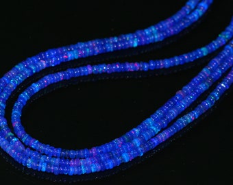 May include: Close-up of three strands of blue opal beads. The beads are small and round, with a vibrant blue color and flashes of pink and green. The strands are arranged in a flowing, layered pattern.