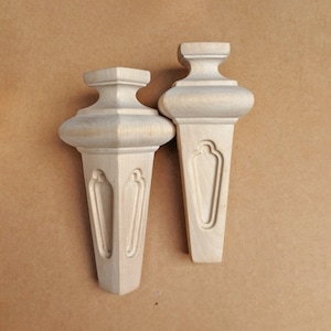 Puede incluir: Dos patas de muebles de madera sin terminar con un diseño decorativo. Las patas son de madera clara y tienen una parte superior redondeada y una parte inferior puntiaguda.