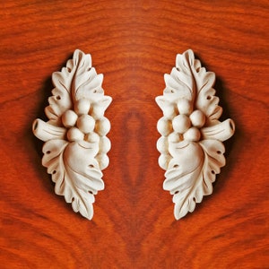 May include: Two white wooden decorative accents shaped like grapevines with leaves and grapes. The accents are on a red wood background.