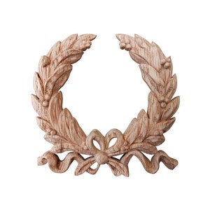 Peut inclure: Une couronne en bois sculptée avec un nœud au centre. La couronne est faite de feuilles et de baies et est de couleur brun clair.