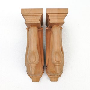 K&ouml;nnte beinhalten: Zwei Holz-Konsolen mit einem geschnitzten Schwanenmotiv. Die Konsolen sind hellbraun und haben ein detailliertes, kunstvolles Design.