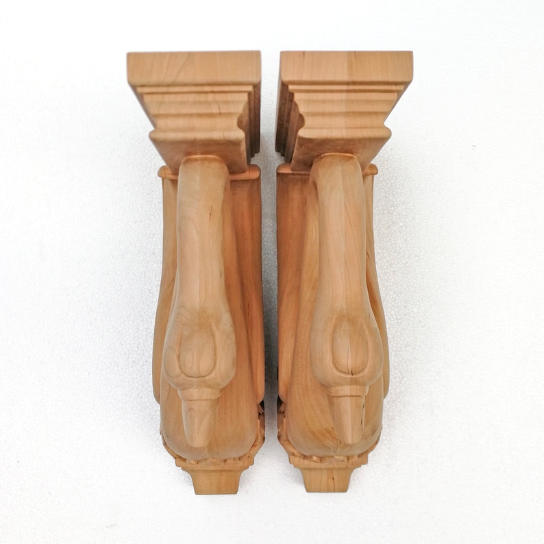 K&ouml;nnte beinhalten: Zwei Holz-Konsolen mit einem geschnitzten Schwanenmotiv. Die Konsolen sind hellbraun und haben ein detailliertes, kunstvolles Design.