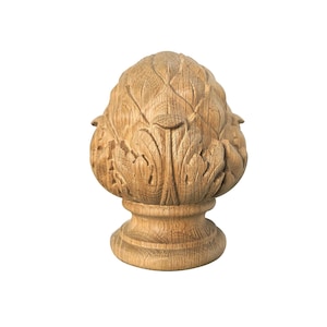 Op de afbeelding: Een gesneden houten finial in de vorm van een dennenappel. De lichtbruine finial heeft gedetailleerde bladsnijwerk en een ronde basis. De houtnerf is zichtbaar, wat textuur en diepte aan het ontwerp toevoegt. Een decoratief element.