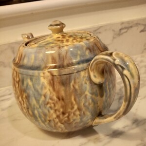 May include: A vintage ceramic teapot with a blue, brown, and yellow glaze. The teapot has a round body and a curved handle.