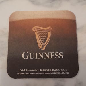May include: Square Guinness coaster with a gradient brown and black background. The Guinness harp logo is in the center, with the word "GUINNESS" below it. Text at the bottom reads "Drink Responsibly. drinkaware.co.uk for the facts."