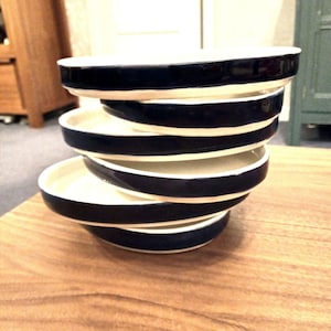 Op de afbeelding: Een stapel van vijf witte keramische kommen met een donkerblauwe rand. De kommen zijn gestapeld op een houten oppervlak.