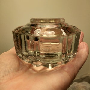 May include: A clear glass inkwell with a faceted design. The inkwell is empty and has a round opening at the top.