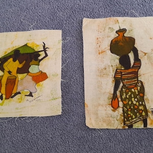 May include: Two small fabric art pieces with African-themed illustrations. One depicts figures dancing with drums, the other a person carrying a pot. The art is in shades of yellow, orange, and brown.