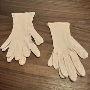 May include: A pair of pale pink, lacy gloves. The gloves are made of a delicate, open-weave fabric.