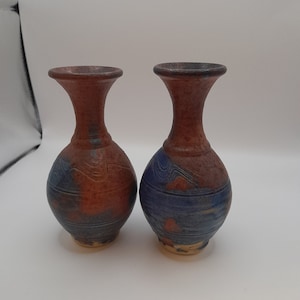 Puede incluir: Dos pequeños jarrones de cerámica con un esmalte azul y marrón. Los jarrones tienen un cuerpo redondeado y un cuello estrecho.