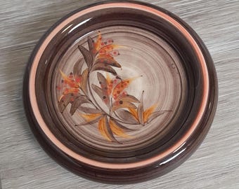 Könnte beinhalten: Eine braune Keramikschale mit einem Wirbelmuster und einem Blumendesign in Orange-, Gelb- und Brauntönen.