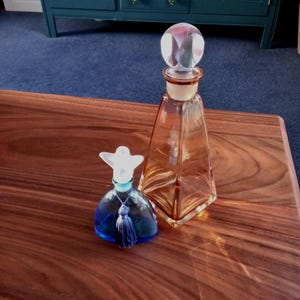 May include: Two glass bottles with stoppers. The larger bottle is amber coloured and has a clear glass stopper. The smaller bottle is blue and has a white stopper with a blue tassel.