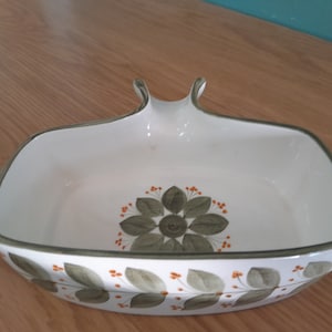 Puede incluir: Plato de servir de cerámica blanca con un diseño floral verde y naranja. El plato tiene una forma única con un asa en la parte superior.